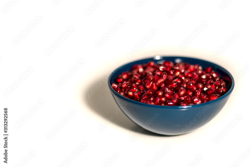 blue plate full of pomegranate seeds on a white background, isolate, side view blue plate full of pomegranate seeds on a white background, isolate, side view