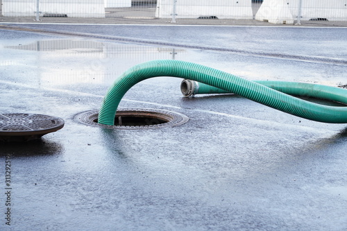the green thick hose from a sewer pit, pumping sewage or sewage from collector in city. water drainage. Sewer manhole with an open manhole cover and large corrugated suction hoses for waste disposal photo