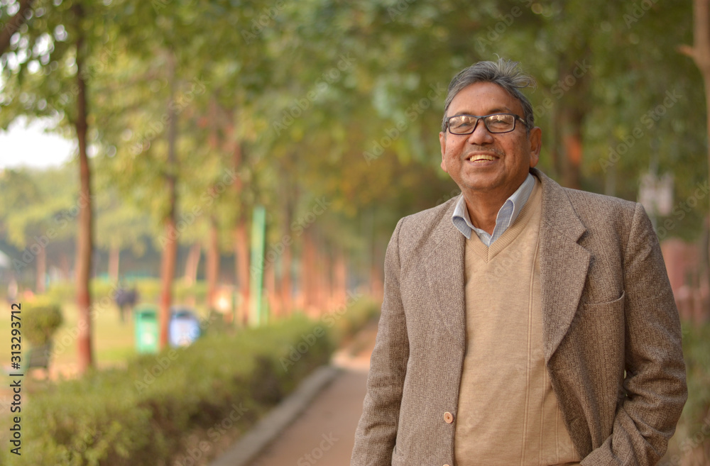 Portrait of a happy senior Indian man wearing a tweet suit/coat in the outside setting standing and thinking in a park in winters in New Delhi, India Portrait of a happy senior Indian man wearing a tweet suit/coat in the outside setting standing and thinking in a park in winters in New Delhi, India