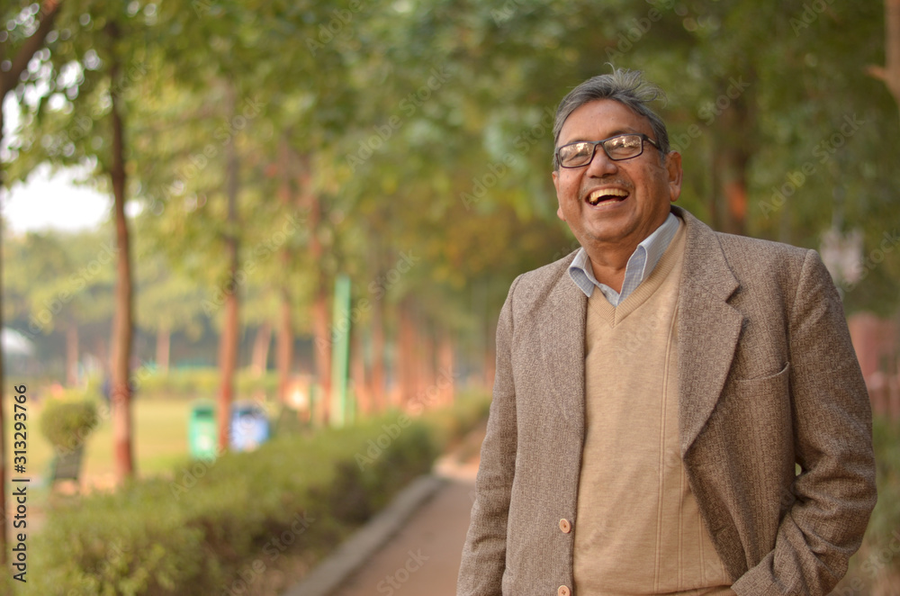 Happy senior Indian man wearing a suit standing and laughing in a park wearing tweed coat in winters in New York, USA Happy senior Indian man wearing a suit standing and laughing in a park wearing tweed coat in winters in New York, USA