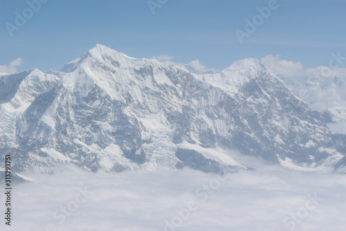 A beautiful photo of a mountain with glacier and snow on it from a height above the clouds © UTKARSH
