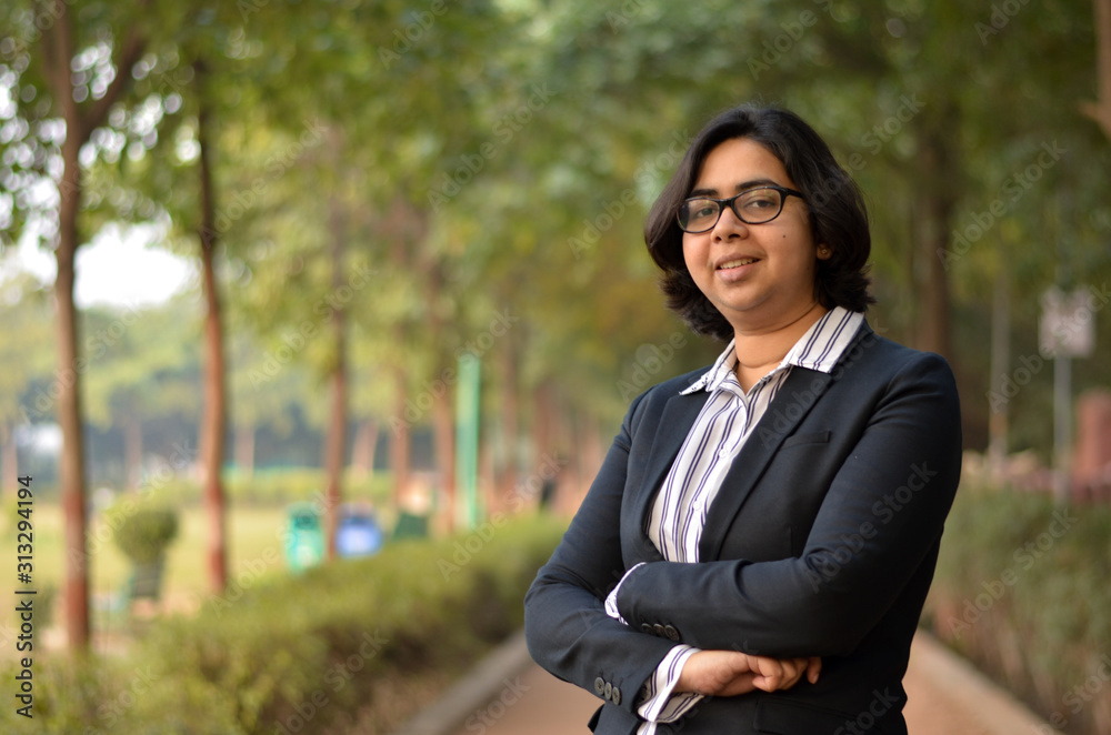 Closeup portrait of a confident young Indian Corporate professional woman with short hair and spectacles, holding a laptop in hands in an outdoor setting wearing a black white stripped shirt in a park Closeup portrait of a confident young Indian Corporate professional woman with short hair and spectacles, holding a laptop in hands in an outdoor setting wearing a black white stripped shirt in a park