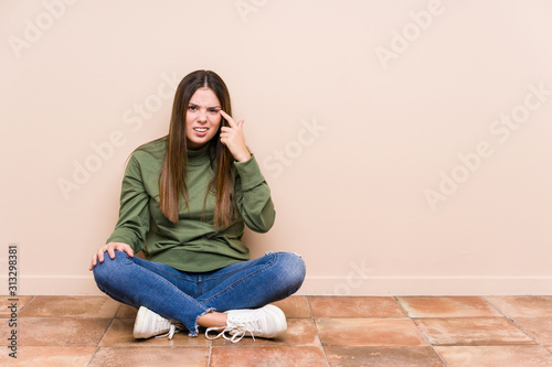 Young caucasian woman sitting on the floor isolated showing a disappointment gesture with forefinger. © Asier