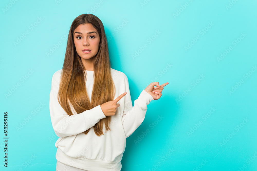 Fototapeta premium Young slim woman shocked pointing with index fingers to a copy space.