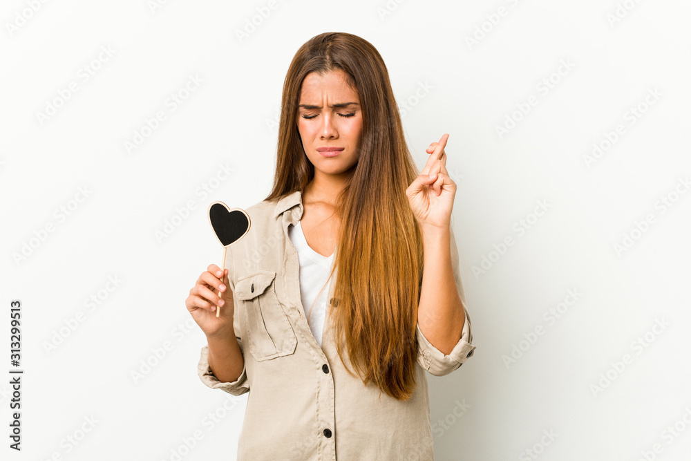 Young caucasian woman holding a heart shape crossing fingers for having luck Young caucasian woman holding a heart shape crossing fingers for having luck