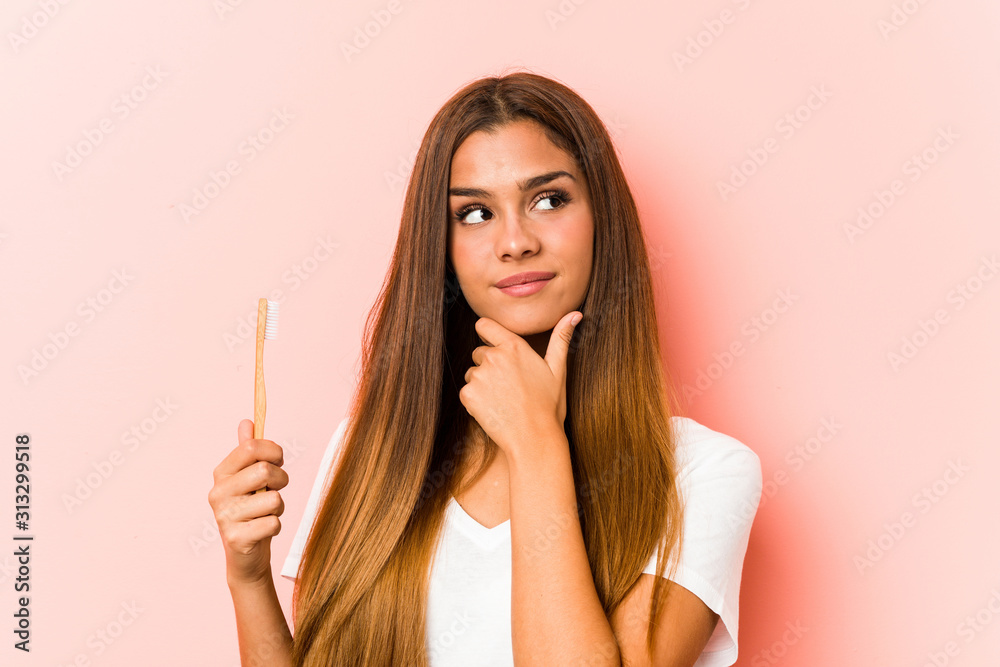 Young caucasian woman holding a toothbrush looking sideways with doubtful and skeptical expression. Young caucasian woman holding a toothbrush looking sideways with doubtful and skeptical expression.