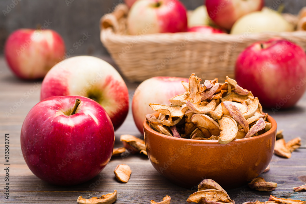 Dried apples in slices in a bowl and fresh apples on a wooden table Dried apples in slices in a bowl and fresh apples on a wooden table