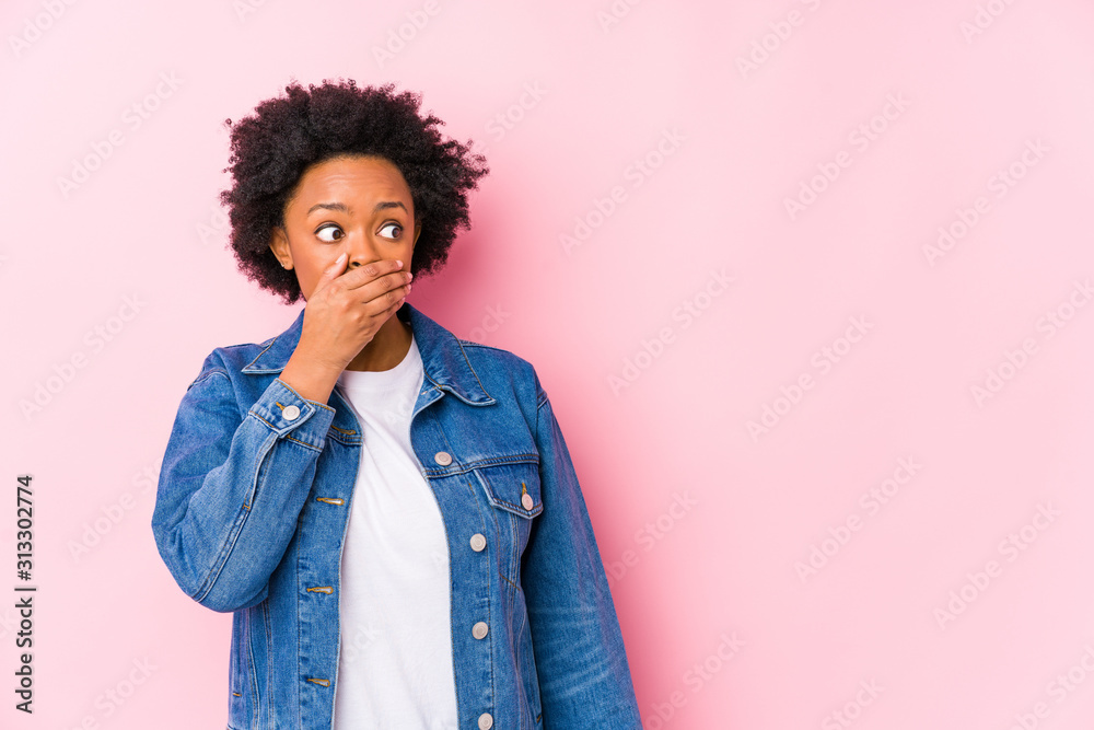 Young african american woman against a pink backgroound isolated thoughtful looking to a copy space covering mouth with hand. Young african american woman against a pink backgroound isolated thoughtful looking to a copy space covering mouth with hand.