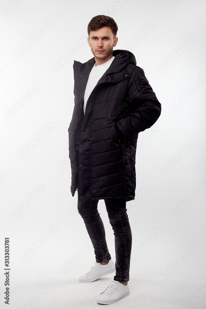 Young european man in white sweater and black pants, black down jacket posing on white background. Isolated. Young european man in white sweater and black pants, black down jacket posing on white background. Isolated.