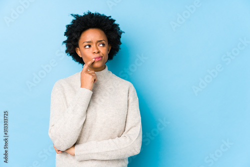 Middle aged african american woman against a blue background isolated looking sideways with doubtful and skeptical expression.
