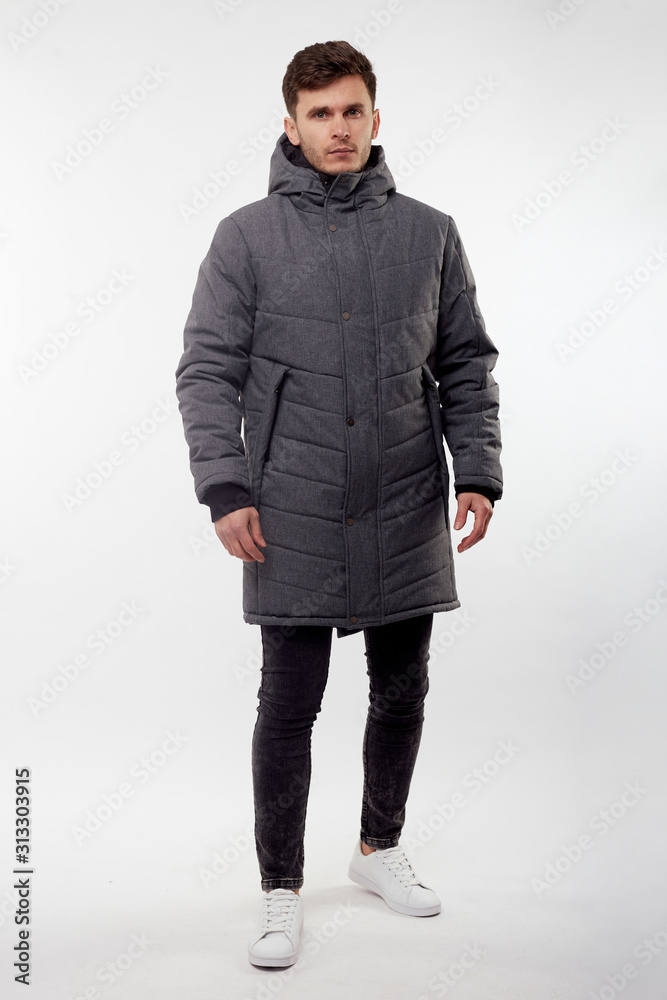 Young european man in white sweater and black pants, gray down jacket posing on white background. Isolated. Young european man in white sweater and black pants, gray down jacket posing on white background. Isolated.