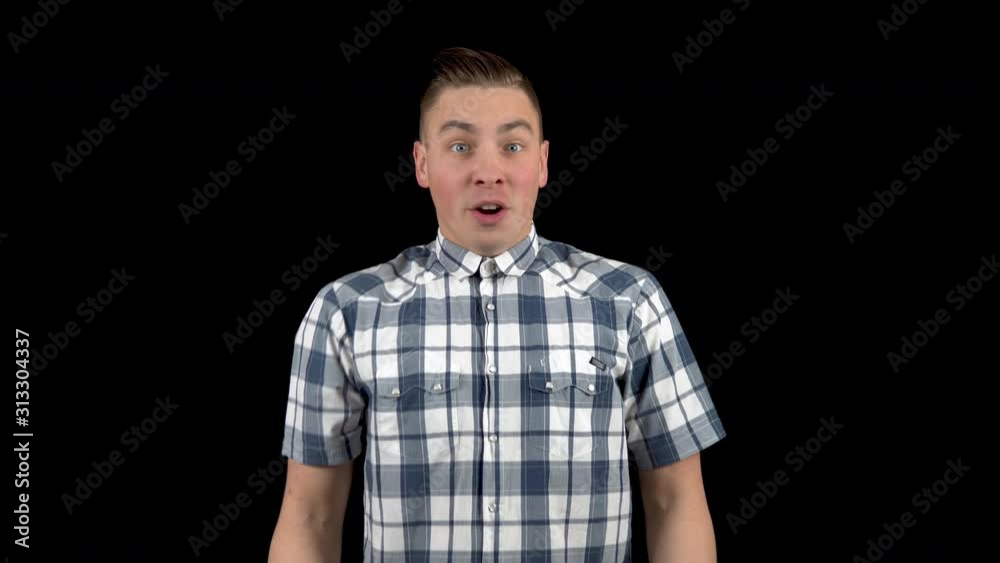 The young man shows emotions of surprise on his face. Surprised man in a shirt on a black background. The young man shows emotions of surprise on his face. Surprised man in a shirt on a black background.