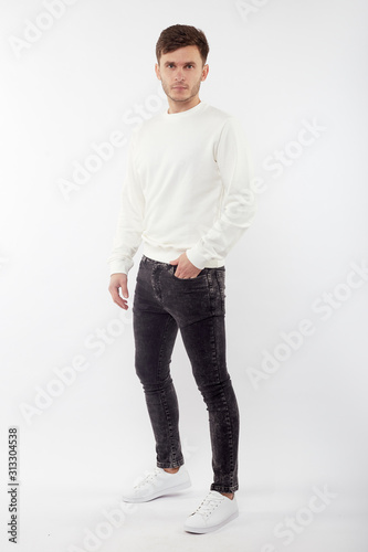 Young european man in white sweater and black pants posing on white background. Isolated.