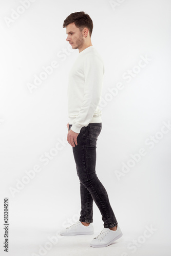 Young european man in white sweater and black pants posing on white background. Isolated. © Alexey