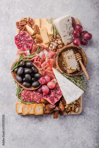 Traditional italian antipasto plate. Assorted cheeses on wooden cutting board. Brie cheese, cheddar slices, gogonzola, walnuts grapes, olives, prosciutto, rosemary and glass of red wine. top view
