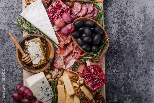 Traditional italian antipasto plate. Assorted cheeses on wooden cutting board. Brie cheese, cheddar slices, gogonzola, walnuts grapes, olives, prosciutto, rosemary and glass of red wine. top view photo