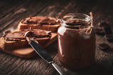 Close up of jar of chocolate nut cream and slices of bread with pasta on wooden background