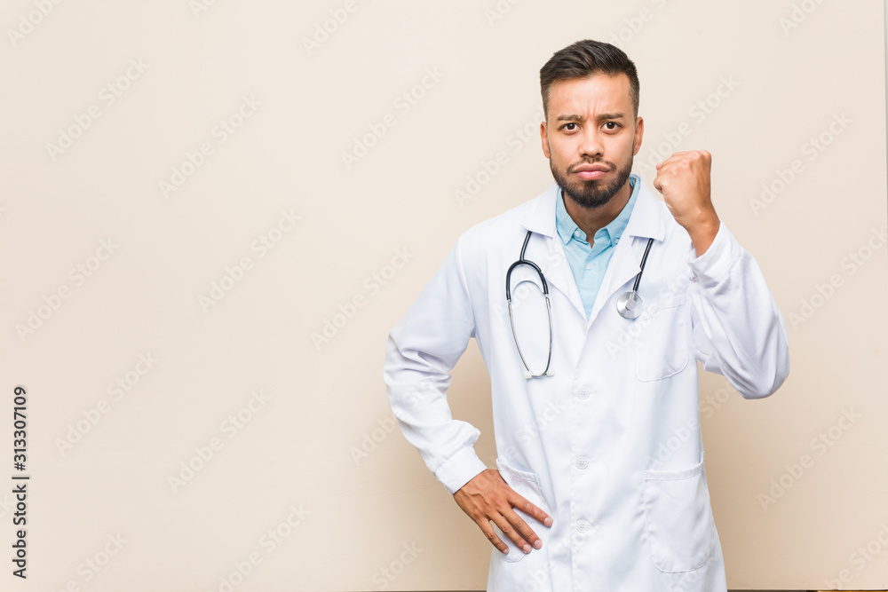 Young south-asian doctor man showing fist to camera, aggressive facial expression. Young south-asian doctor man showing fist to camera, aggressive facial expression.