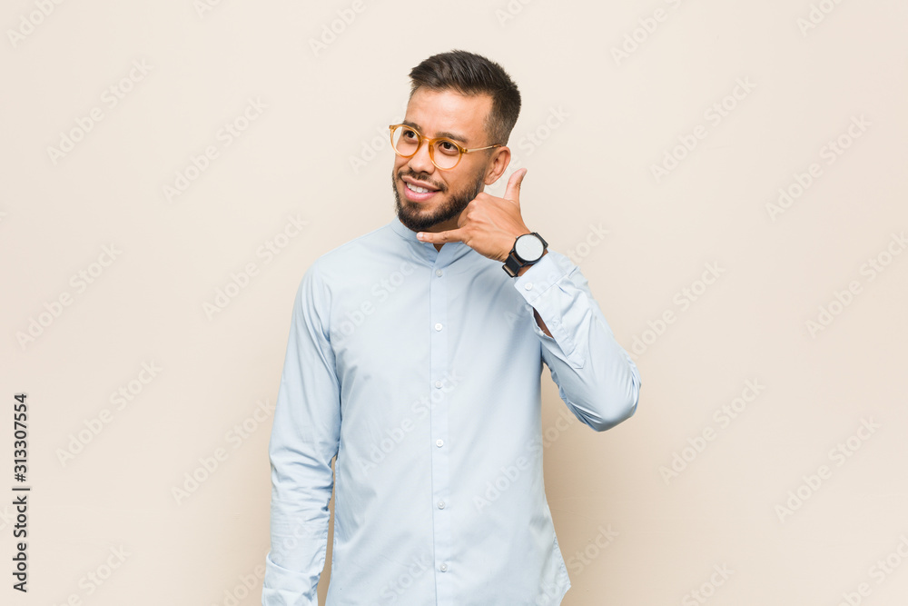 Young south-asian business man showing a mobile phone call gesture with fingers. Young south-asian business man showing a mobile phone call gesture with fingers.