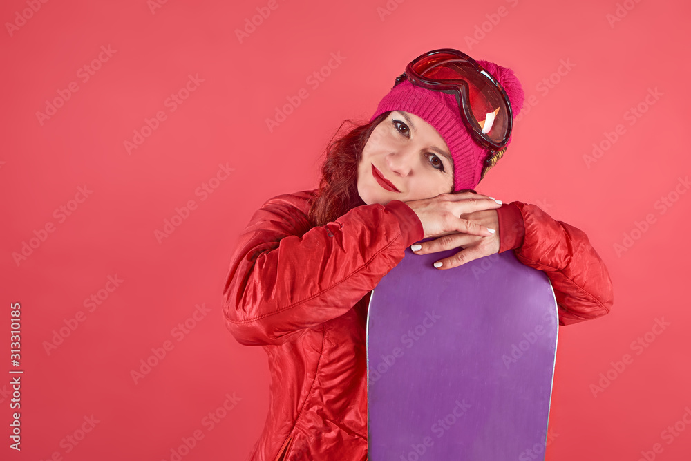 Studio shot woman in rad wearing ski clothes standing in red background with snowboard and ski mask Studio shot woman in rad wearing ski clothes standing in red background with snowboard and ski mask