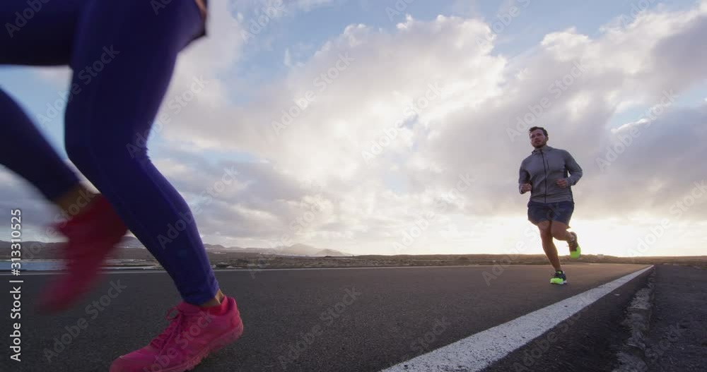 Two runners running on road training for marathon run outside at sunset. Woman and man living healthy lifestyle outdoors.