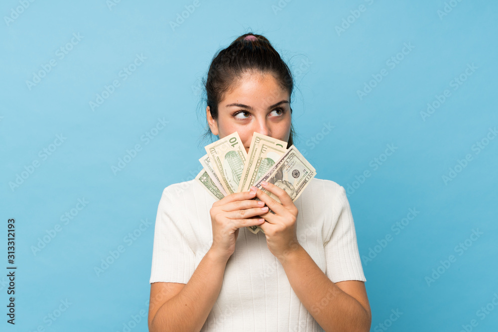 Young brunette girl over isolated blue background taking a lot of money Young brunette girl over isolated blue background taking a lot of money
