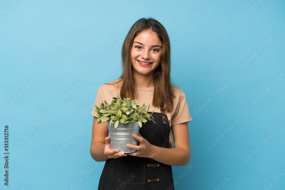 Young brunette girl over isolated blue background taking a flowerpot Young brunette girl over isolated blue background taking a flowerpot