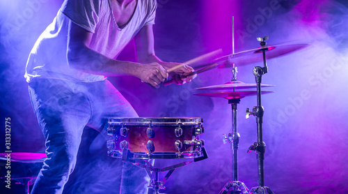 A drummer plays drums on a blue background. Beautiful special effects of light and smoke. The process of playing a musical instrument.