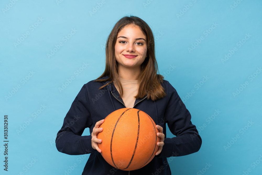 Young brunette girl over isolated blue background with ball of basketball