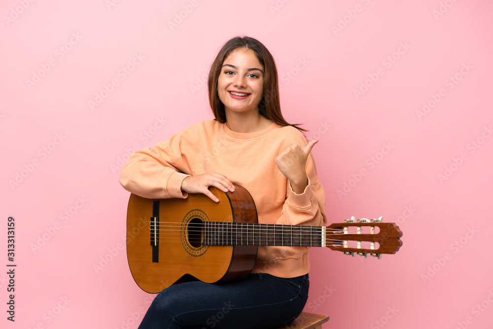 Young brunette girl with guitar over isolated pink background with thumbs up because something good has happened Young brunette girl with guitar over isolated pink background with thumbs up because something good has happened