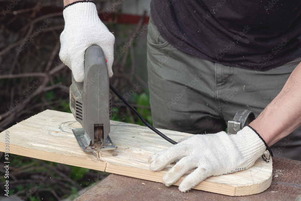 Carpenter sawing a wooden plank by a jigsaw.