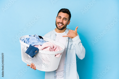 Fotografie, Obraz Young handsome man doing laundry isolated showing a mobile phone call gesture with fingers