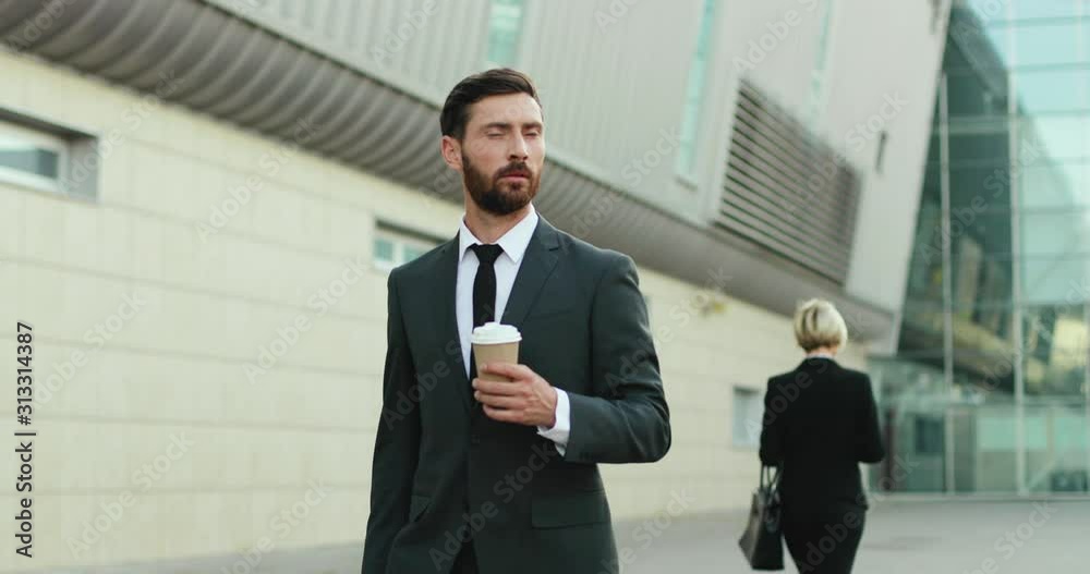 Caucasian handsome successful businessman walking outside to the work in the morning and drinking coffee to-go, woman passing by. Caucasian handsome successful businessman walking outside to the work in the morning and drinking coffee to-go, woman passing by.