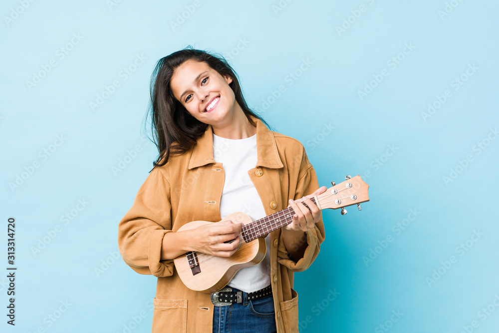 Young caucasian woman playing ukelele isolated on a blue background Young caucasian woman playing ukelele isolated on a blue background