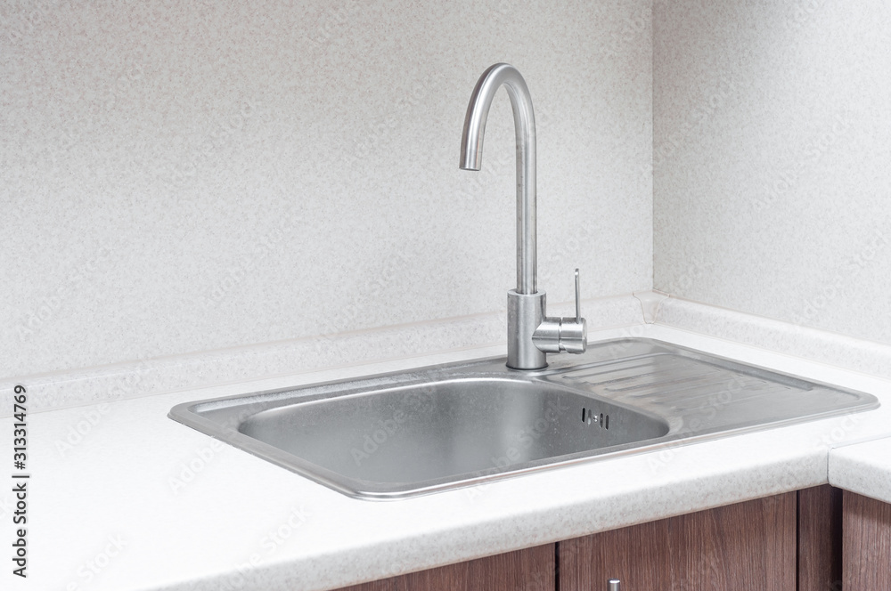 Iron washbasin with tap and spout embedded in a wooden kitchen worktop. Corner wash in the interior and design of a modern minimalist kitchen.