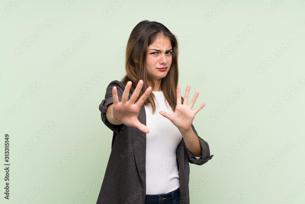 Young brunette girl with blazer over isolated green background nervous stretching hands to the front Young brunette girl with blazer over isolated green background nervous stretching hands to the front