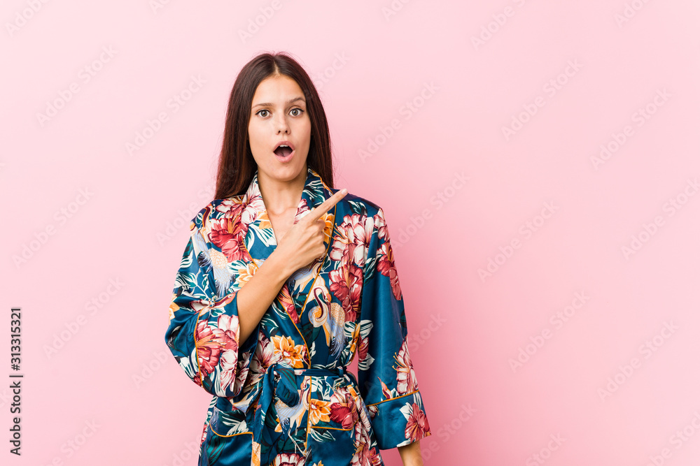 Young caucasian woman wearing a kimono pajama pointing to the side Young caucasian woman wearing a kimono pajama pointing to the side