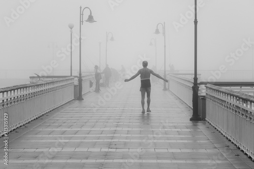 A man resting after his morning jogging routine and enjoying the silence of the misty bridge full of fishermen