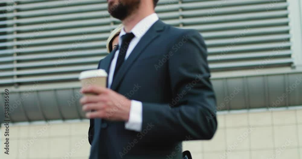 Caucasian young businesswoman standing outside like waiting for somebody with a phone in hands while tapping and texting on it. Man in business style passing by with a coffee to-go in the morning. Caucasian young businesswoman standing outside like waiting for somebody with a phone in hands while tapping and texting on it. Man in business style passing by with a coffee to-go in the morning.