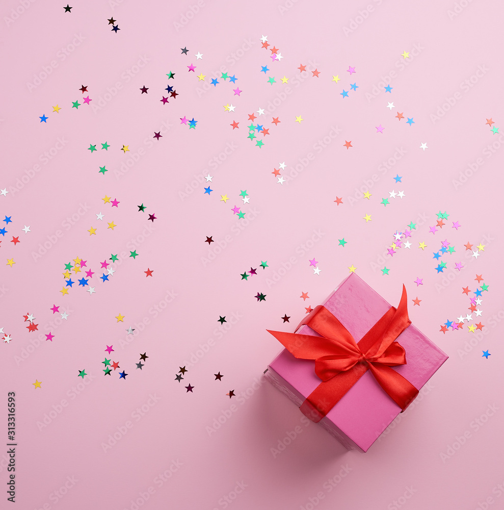 beautiful pink closed box with a big bow on a pink background with multi-colored sparkles beautiful pink closed box with a big bow on a pink background with multi-colored sparkles