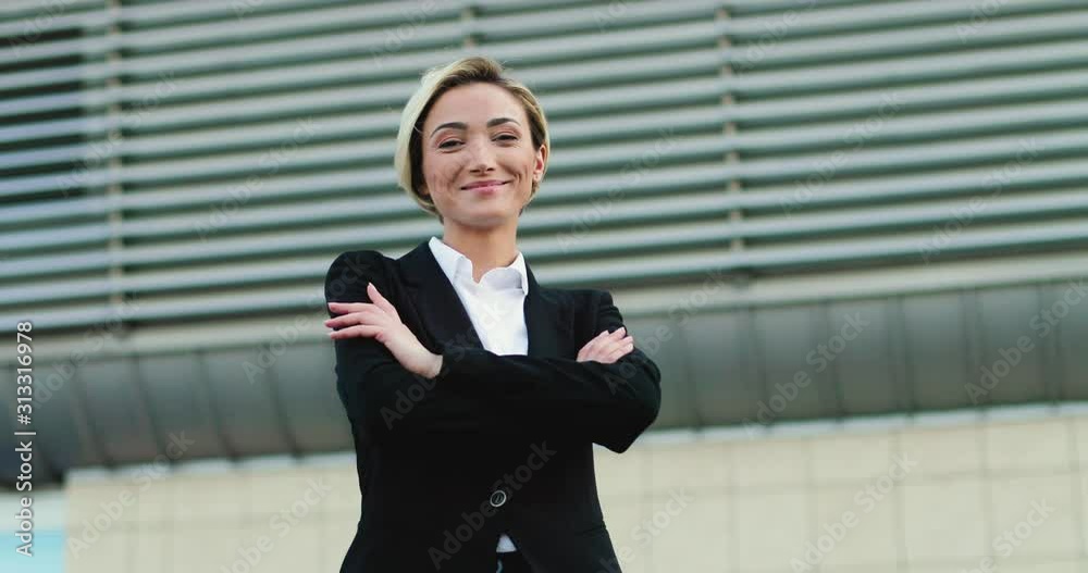 Portrait of the cheerful Caucasian pretty businesswomanwith fair hair smiling happily to the camera outdoors and crossing hands in front. Portrait of the cheerful Caucasian pretty businesswomanwith fair hair smiling happily to the camera outdoors and crossing hands in front.
