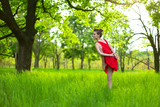 Young sports girl in a red dress practices yoga in a quiet green forest. Meditation and oneness with nature