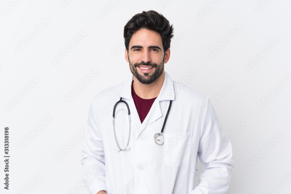 Young handsome man with beard over isolated white background wearing a doctor gown and with stethoscope