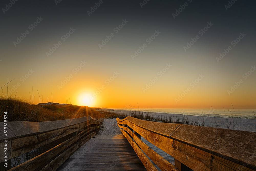 Warm sunrise casting a soft glow on the wooden walkway at the beach