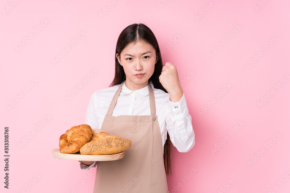 Young chinese baker woman isolated showing fist to camera, aggressive facial expression. Young chinese baker woman isolated showing fist to camera, aggressive facial expression.