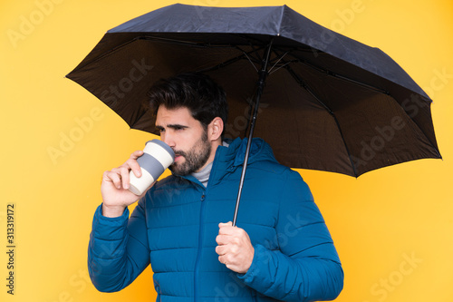 Man holding an umbrella over isolated yellow background © luismolinero