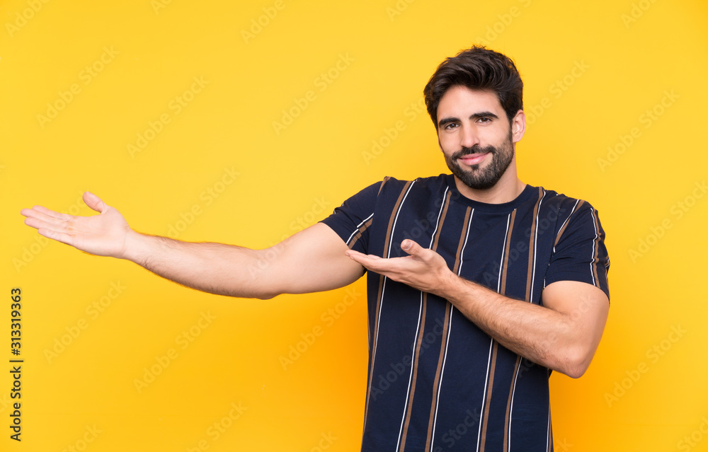 Young handsome man with beard over isolated yellow background extending hands to the side for inviting to come Young handsome man with beard over isolated yellow background extending hands to the side for inviting to come