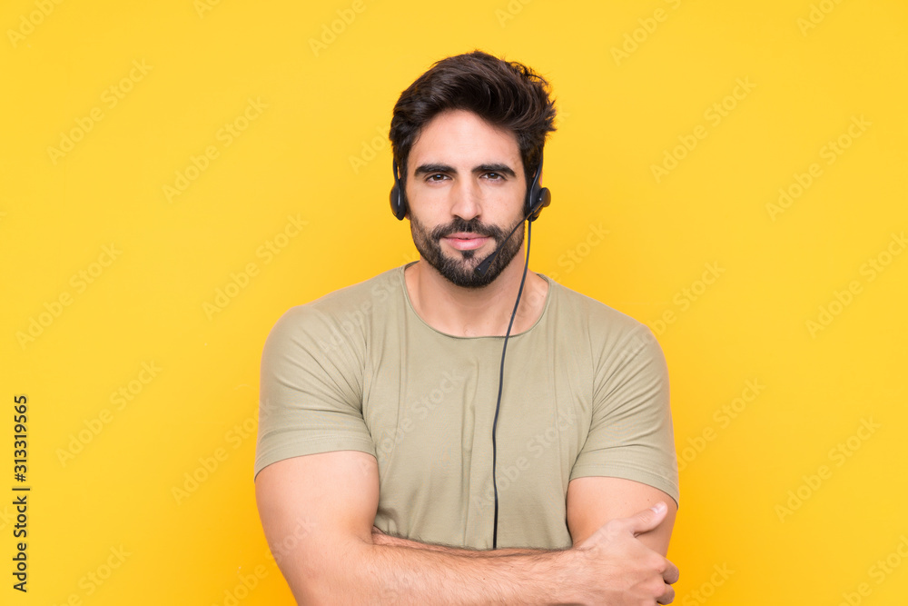 Telemarketer man working with a headset over isolated yellow background keeping arms crossed