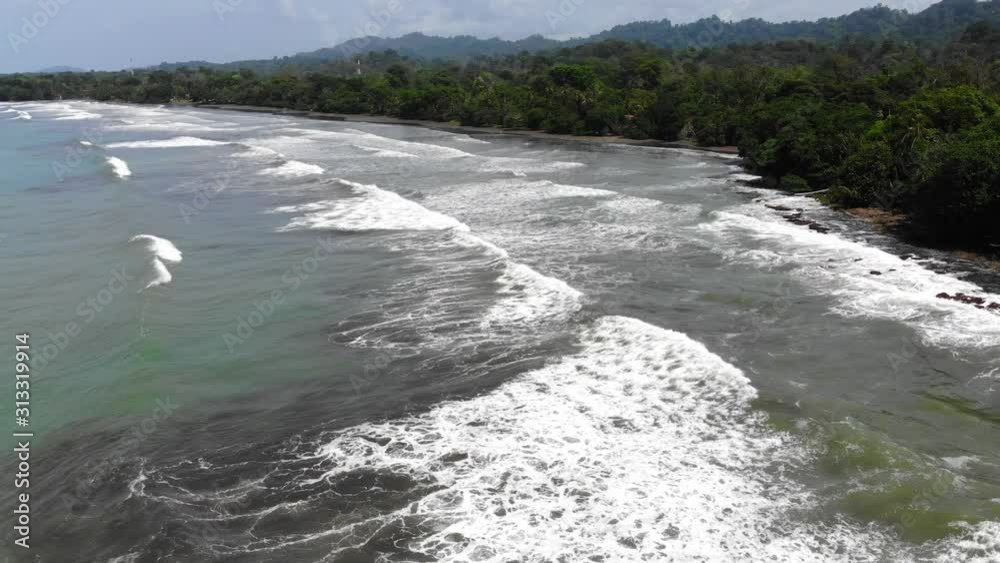 Aerial shot of the ocean waves at Cahuita, Costa Rica. Shot starting from the green coast of Cahuita, flying backwards shot. Aerial shot of the ocean waves at Cahuita, Costa Rica. Shot starting from the green coast of Cahuita, flying backwards shot.