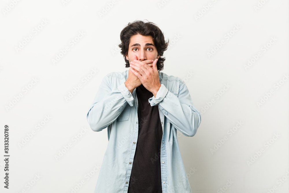 Young handsome man against a white background shocked covering mouth with hands. Young handsome man against a white background shocked covering mouth with hands.
